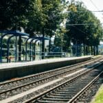 Peron kolejowy otoczony zielenią na obrzeżach dużego miasta